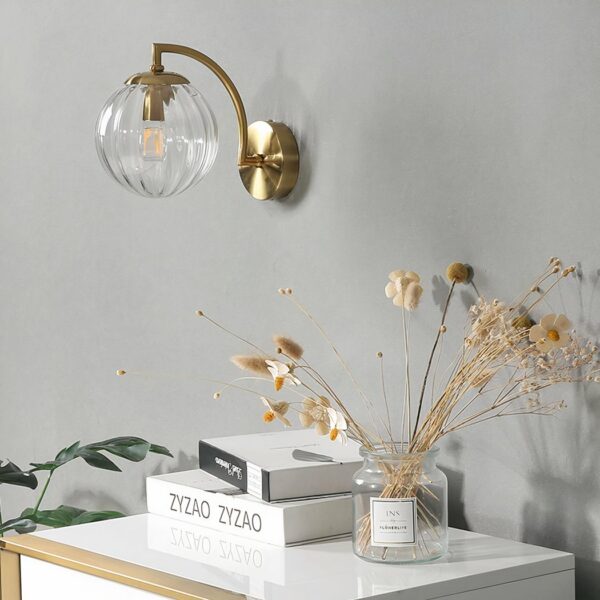 Glass wall light in the shape of a transparent ball, with a gilded bracket above a bedside table