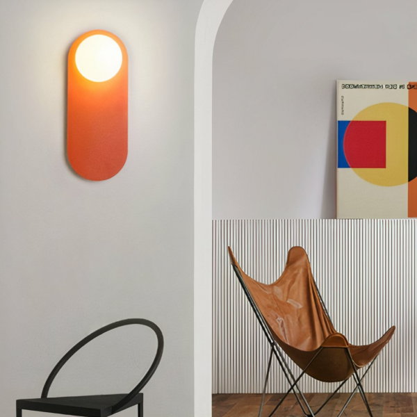 Design orange wall light, in a streamlined room next to an artist's painting and a chair