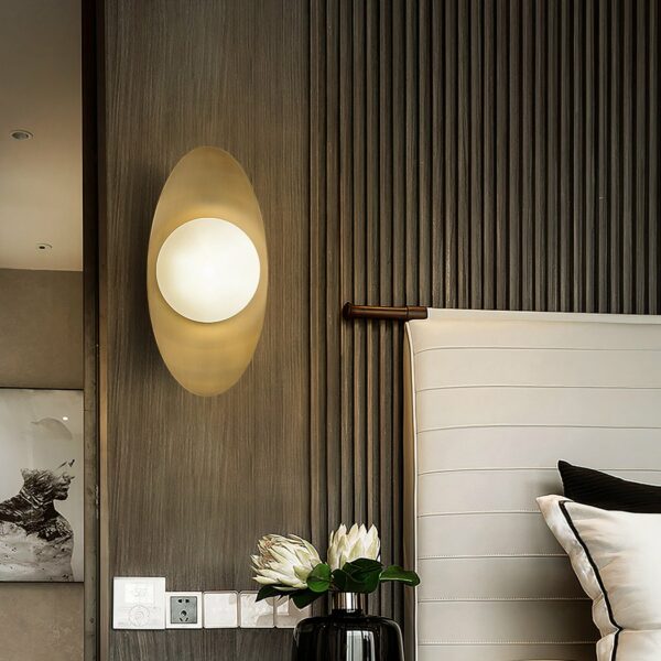 Elegant copper wall light, gold color with a ball on top that sends light, next to a bed in a bedroom