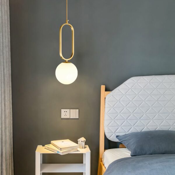Gold-plated hanging lamp in modern glass stone design on a grey background with a bed on the right