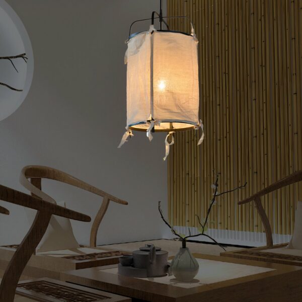 Linen lantern-style pendant with black frame, with light on, above a table