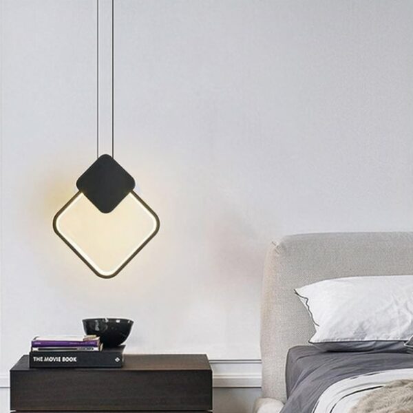 Minimalist black diamond-shaped LED suspension above a bedside table next to a bed