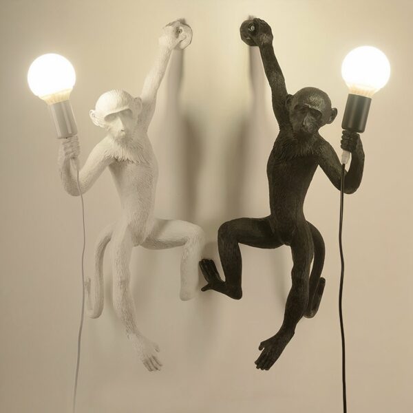 On a white background are two monkey-shaped wall sconces. The one on the right is black and the one on the left is white.