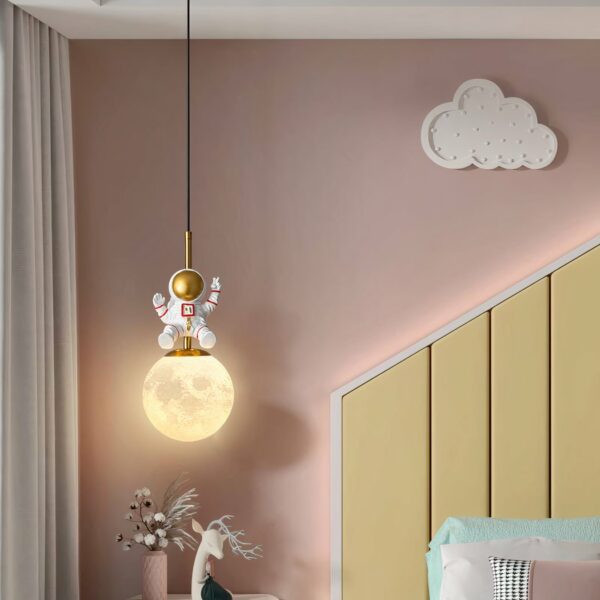 Hanging baby room lamp in the shape of a yellow moon with an astronaut on it in a pink room