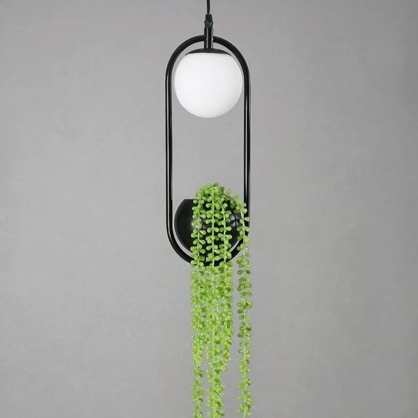 Ceiling lamp, suspended with a white ball at the top and a black ball at the bottom, in which is a fake green plant. The two balls are surrounded by a black stem that connects them. On a gray background.