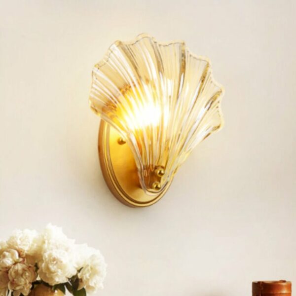 On a white wall, we see a shell-shaped wall application, gold and transparent. A bouquet of white roses can be seen in the bottom left-hand corner.