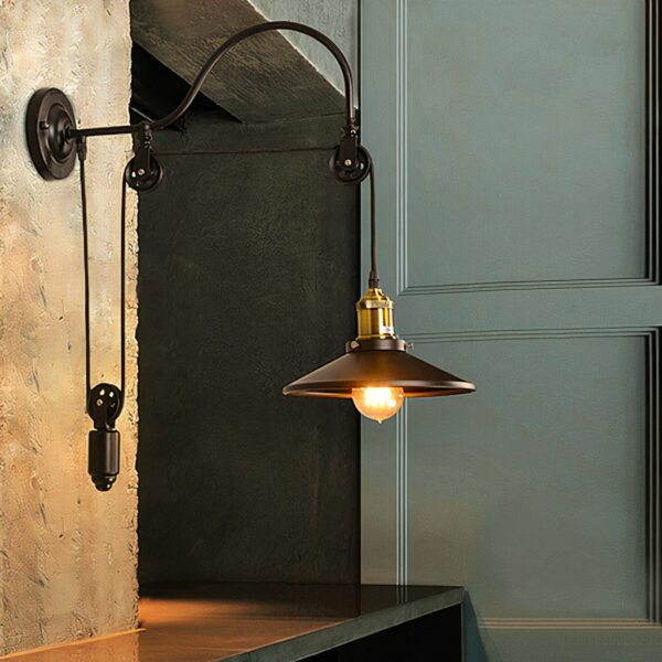 Vintage-style wrought-iron wall light with pulley, black frame, positioned in a dark room next to a door