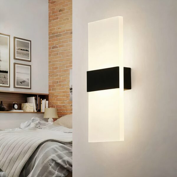 Modern acrylic LED decorative wall light on grey background with bed on the left