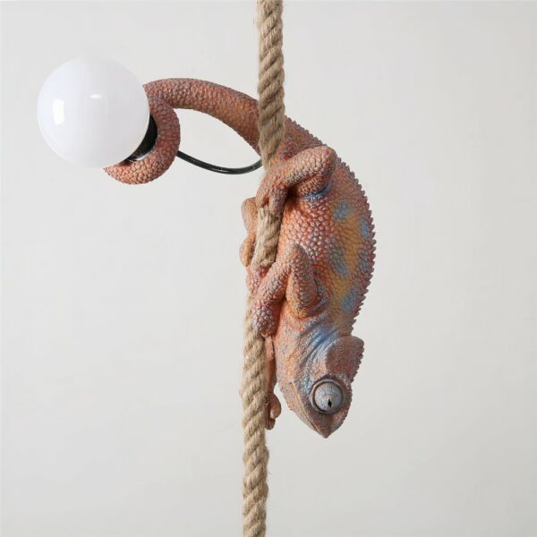 Hanging brown chameleon with blue in places, head down, hanging on a hemp rope. It holds an extinguished light bulb in its tail.