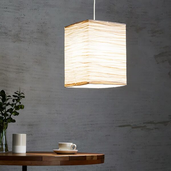Traditional lantern-style Japanese paper hanging suspended in a living room and lit, on a gray background.
