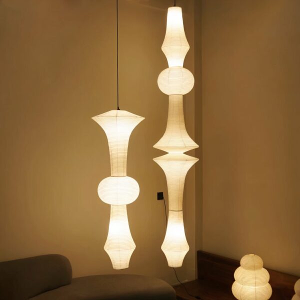 A large white hanging lamp made of Japanese paper, in two versions and lit, in the corner of a living room.