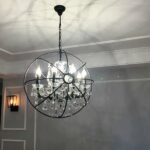 Black orb cage chandelier with crystal candle lights hanging in a hallway