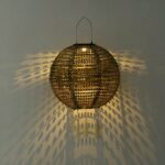 Round woven metal ball lantern lit against a wall casting a dotted shadow
