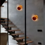 Two eclipse shaped wall lights glowing orange on a staircase wall