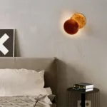 Eclipse shaped wall light glowing warm orange beside a bed