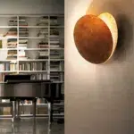 Eclipse shaped wall light glowing golden brown beside a bookshelf