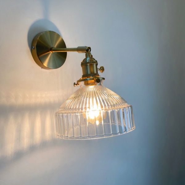 Elegant, modern glass wall sconce with gold-colored base and clear glass shade, with white light