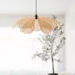 Flower-petal shaped woven pendant light switched on near a window and plant