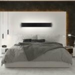 Black linear bar LED wall light glowing above a bed with a dark stone wall