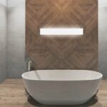 White rectangular LED wall light glowing above a freestanding bathtub