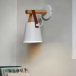 White cone shade wall light hung from a wooden bar by a leather strap