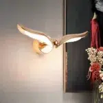Gold bird-shaped wall light switched on beside a framed painting