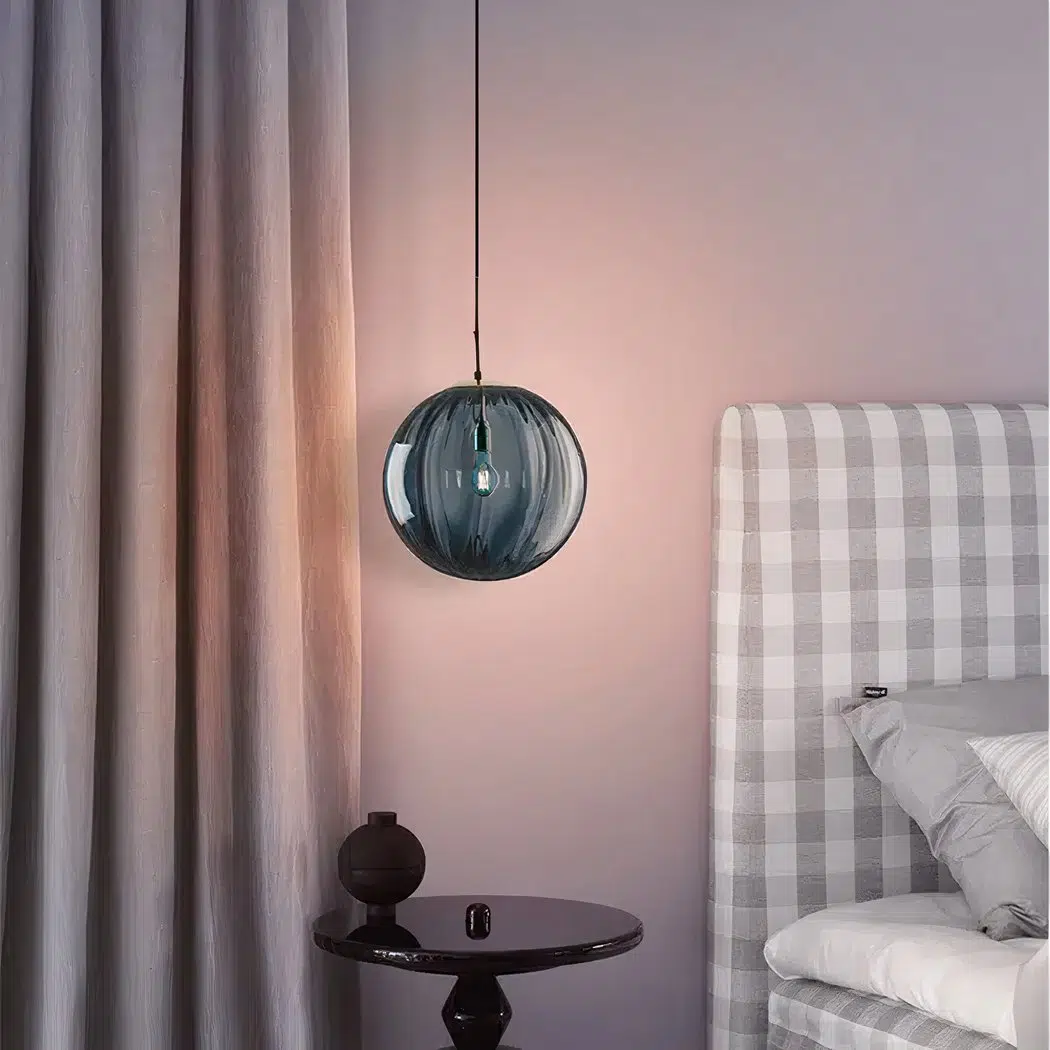 Blue ribbed glass globe pendant light hanging beside a gingham bed headboard