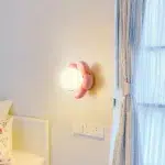 Pink flower-shaped wall light with a white glass globe above a bed
