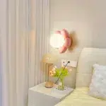 Pink flower-shaped wall light with a white glass globe beside a bedside table