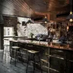 Black cone-shaped pendant lamps in a row above a copper-topped bar counter