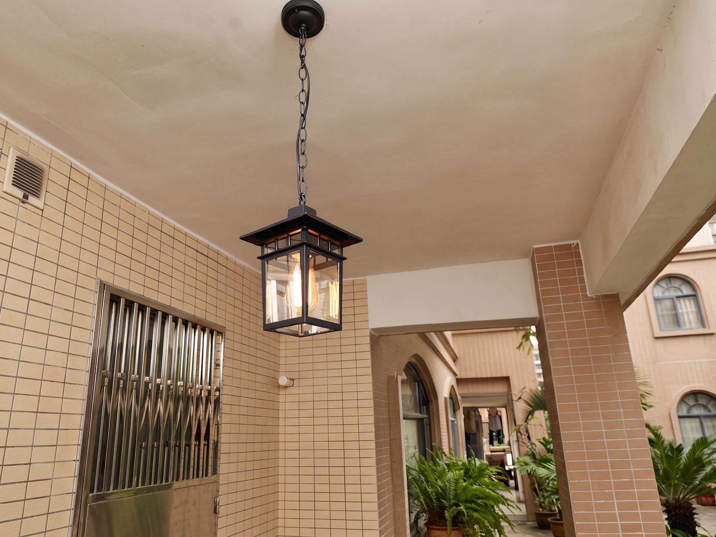 Black lantern pendant on a chain in a tiled outdoor corridor