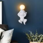 On a dark-blue wall, a white monkey-shaped wall light hangs in the middle.