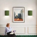 Two green fluted wall lights flanking a framed picture above a woman reading