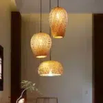 Three woven bamboo pendant lights glowing warm above a beige room with a flower vase