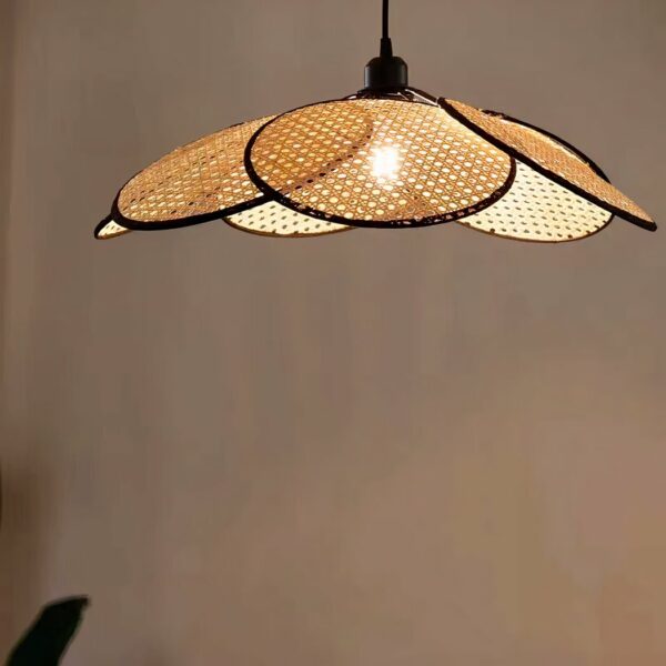 Lustre cannage en forme de fleur, constitué de 6 panneaux mobile disposés autour de l'ampoule allumée. Derrière, on voit un mur beige.