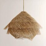 Lustre en paille suspendu, en forme de hutte, recouvert de paille effet brossée. Sur un fond beige.
