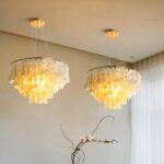 Two mother-of-pearl tiered pendant lamps hanging side by side near a curtain