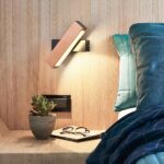 Rectangular wood-toned wall lamp glowing beside a bed with a small succulent nearby
