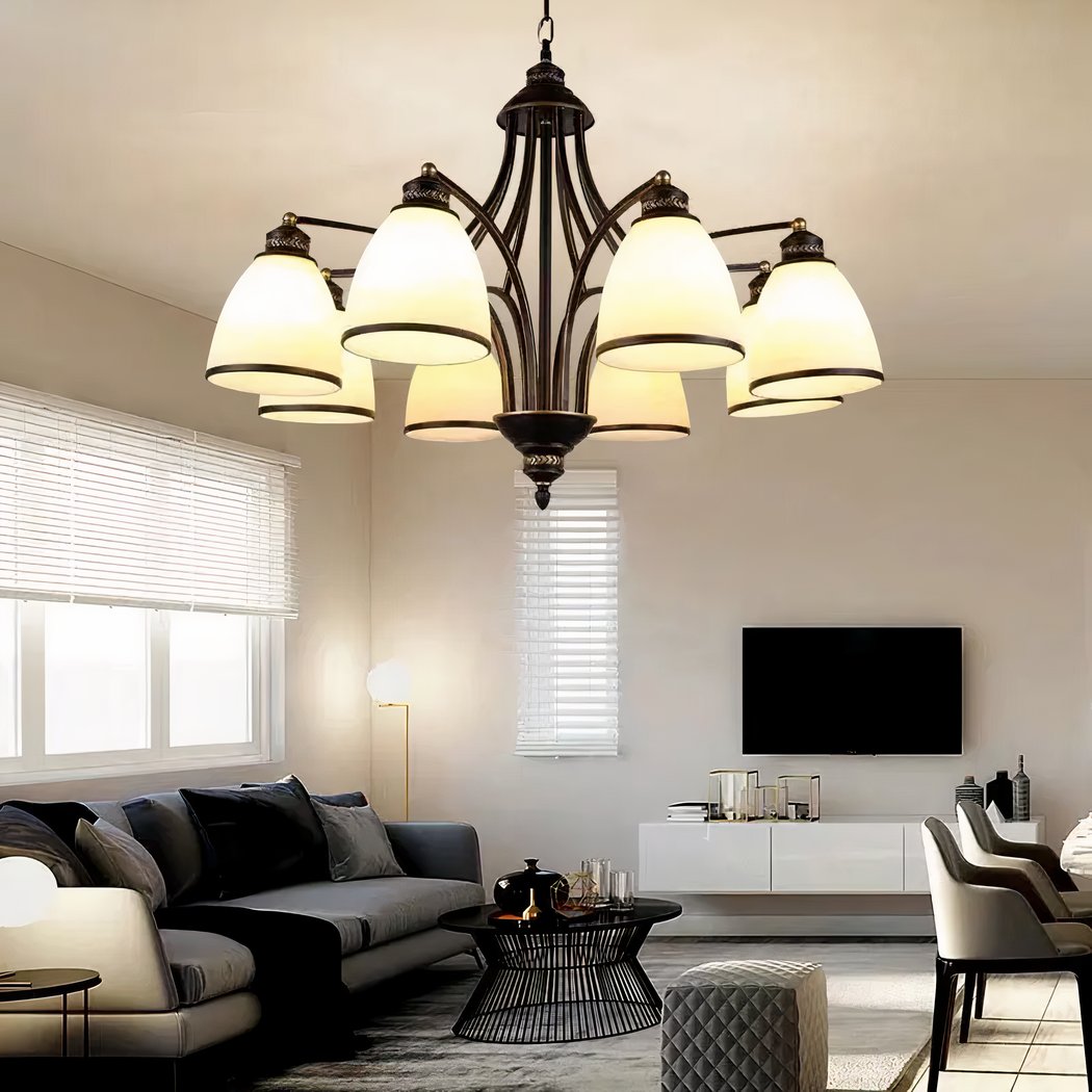 Bronze chandelier with several white bell shaped glass shades above a living room sofa