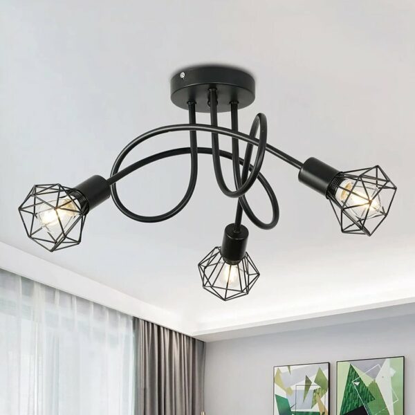 Ceiling chandelier with 3 intertwined black rods with lit bulbs at the ends, with an industrial-style grid surrounding it. On the opposite wall are 2 picture frames, and on the left a window with brown sliding curtain.