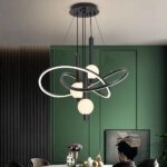 Black LED pendant light with loop shapes in front of a green paneled wall above a table