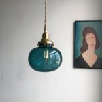 Teal blue glass globe pendant with brass fitting beside a framed portrait