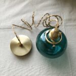 Flat lay of the teal glass globe pendant with its brass ceiling cap and cord