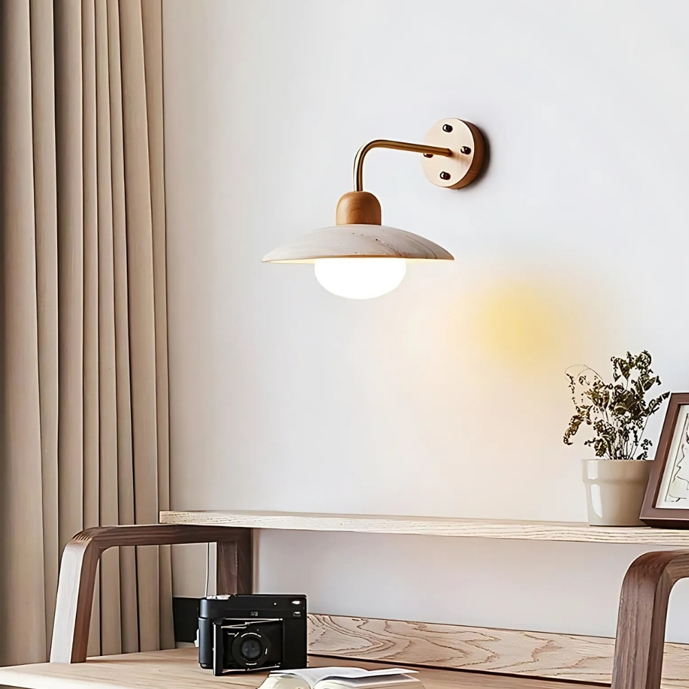 Brass arm wall light with a marbled stone disc shade and glowing globe bulb above a console table