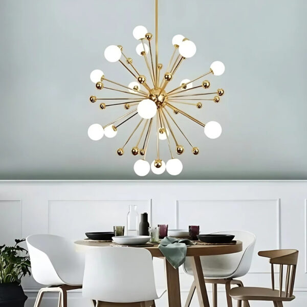 Lustre moderne doré avec boules lumineuses au-dessus d'une table ronde en bois avec quatre chaises autour de celle-ci. En fond, un mur gris et blanc.