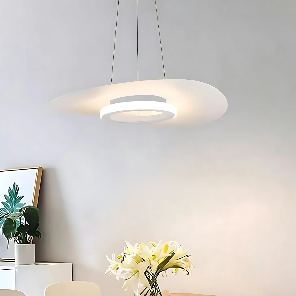 White oval ring-shaped LED pendant hanging low above a table with white lilies