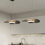 Two flat disc pendants glowing above a kitchen counter with a marble backsplash