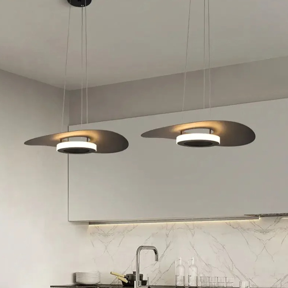 Two flat disc pendants glowing above a kitchen counter with a marble backsplash