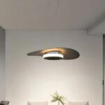 Single flat disc pendant glowing above a dining table against a plain wall
