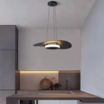 Flat disc pendant glowing above a dark kitchen counter and sink